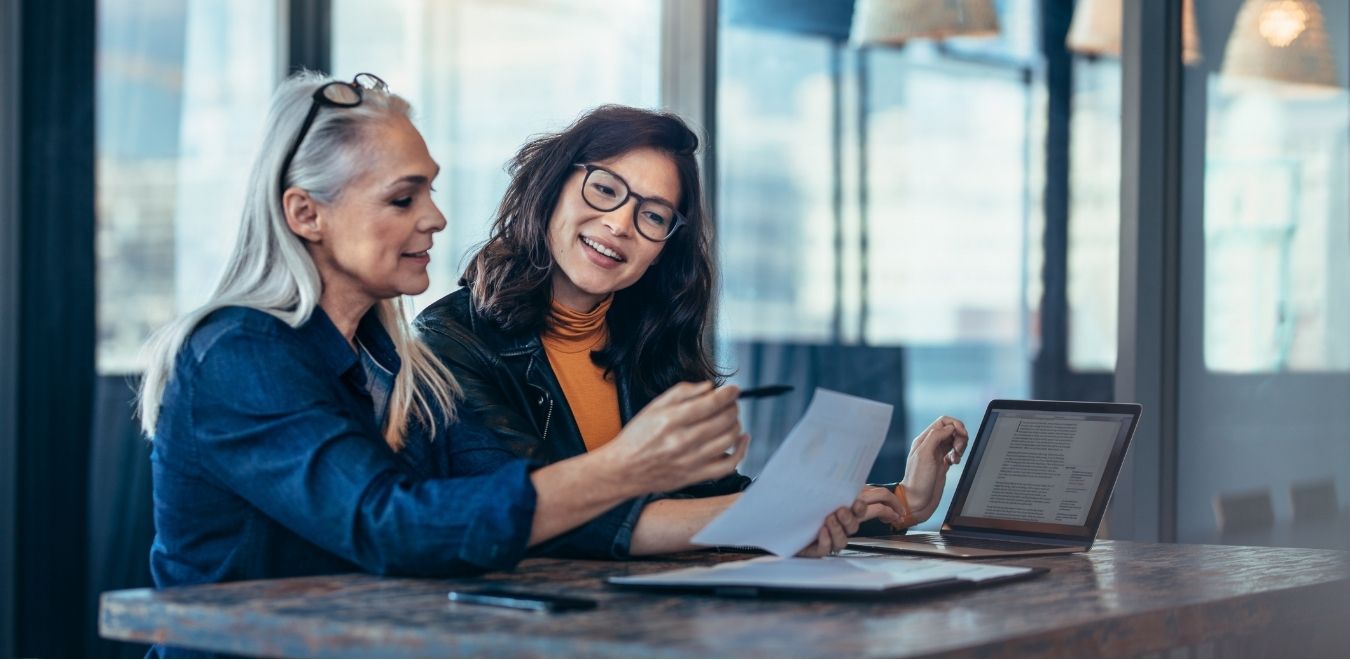 deux femmes sont devant un ordinateurs en train de s'aider à faire leur bilan comptable