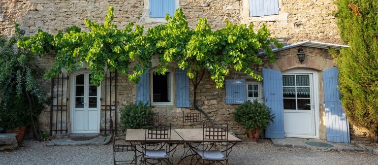 Extérieur d'une maison bourguignonne à volets bleu clair avec glycine au dessus de la porte et table de jardin
